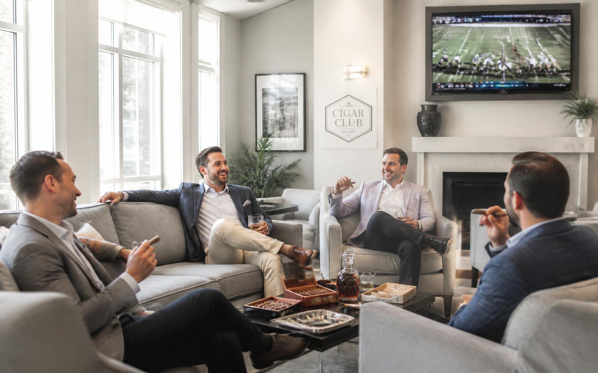 Friends relaxing with cigars and drinks in the bright Perfecto Lounge seating area while a game plays on a large TV